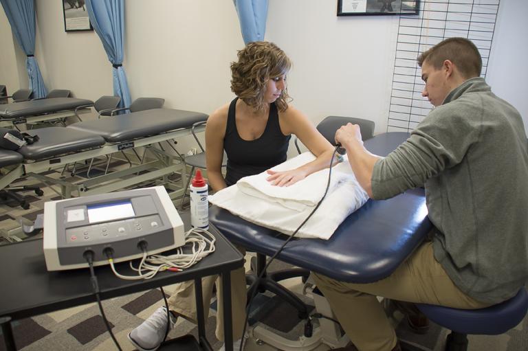 A physical therapy student using a tool on another student